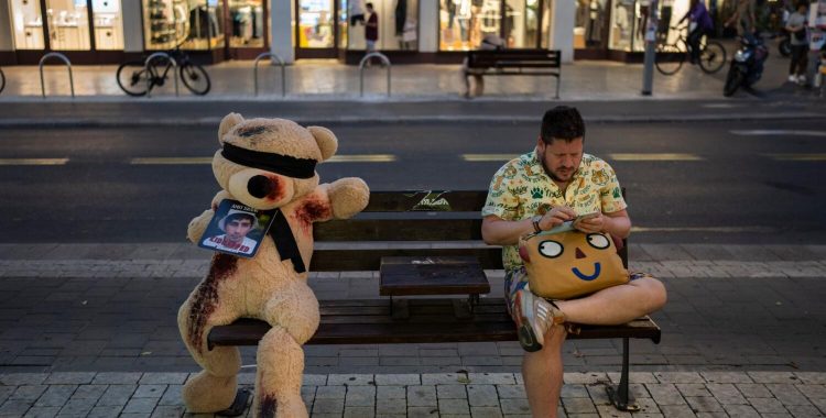 A man sits next to an installation of a blindfolded giant teddy bear in Tel Aviv, Israel, Monday, Nov. 6, 2023. The installation is meant to draw attention to over 240 people who were abducted during the Hamas cross-border attack on Oct. 7. (AP Photo/Bernat Armangue)